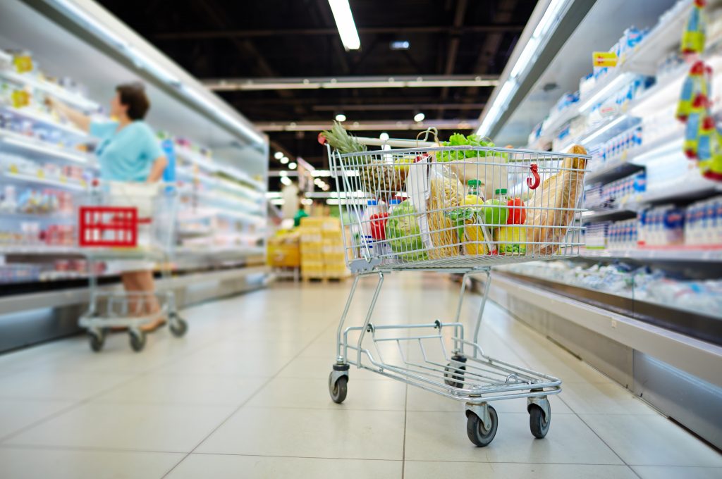 Shopping cart full of grocery standing next to shelves with dairy products in hypermarket